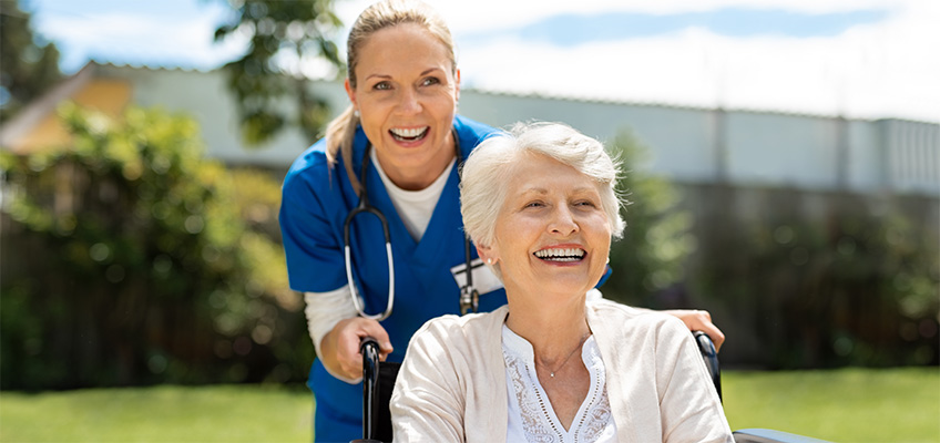 A nurse taking a patient out for a stroll outdoors.